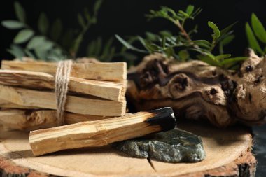 Palo santo çubukları, yanmış bir tane, değerli taş, kapan ve yeşil dal masanın üzerinde, yakın plan.