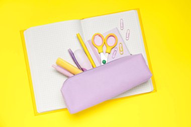 Kalem kutusu ve sarı arkaplanda farklı kırtasiye malzemesi, üst görünüm