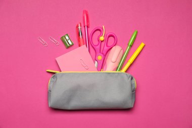 Kalem kutusu ve pembe arka planda farklı kırtasiye malzemesi, düz konum