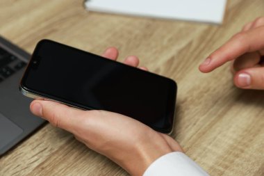 Adam ahşap masada boş ekranlı akıllı telefon kullanıyor.