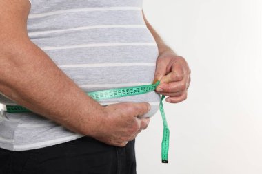 Kilolu bir adam göbeğini beyaz arka planda bantla ölçüyor, yakın plan. Metin için boşluk