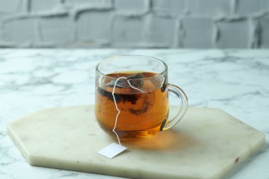 Cam bardakta çay poşeti, hafif mermer masada sıcak içecek.