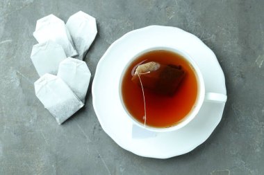 Çay poşetleri ve bardakta sıcak içecek gri desenli masa, düz uzanmış