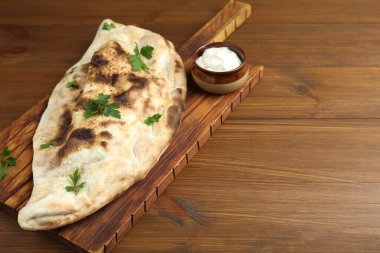Lezzetli calzone, maydanoz ve soslu tahta masa, yakın plan. Metin için boşluk