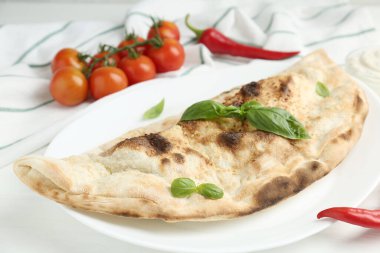 Lezzetli calzone, fesleğen, biber ve domatesler beyaz ahşap masada, yakın plan.