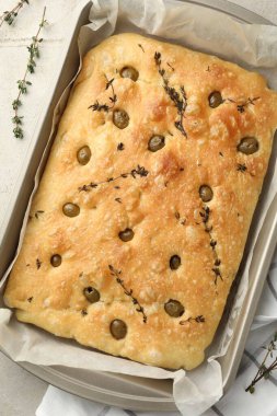 Zeytinli ve kekikli enfes Focaccia ekmeği açık gri masada, üst görünümde.