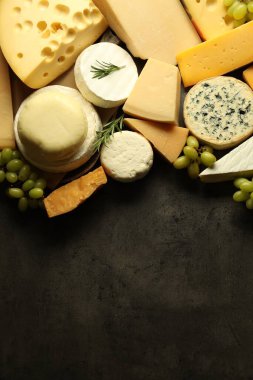 Farklı peynir türleri, biberiye ve üzümler koyu dokulu masa, düz yatak. Metin için boşluk