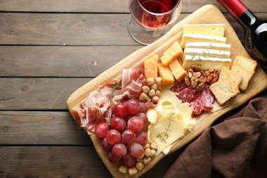 Farklı kesim peynirleri ve ahşap masada şarap ile servis edilen diğer atıştırmalıklar. Metin için boşluk