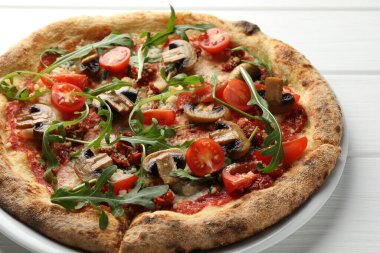 Beyaz ahşap masada mantarlı, domatesli ve roka aromalı lezzetli pizza.
