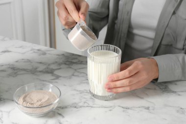 Protein kokteyli yapıyorum. Beyaz mermer masada sütlü bardağa toz ekleyen kadın, yakın plan.