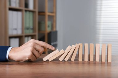 Domino etkisi. Masada tahta blokları iten adam, yakın plan.