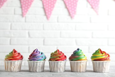 Beyaz tuğla duvarın yanındaki gri desenli masada renkli kremalı lezzetli kekler, yakın plan. Metin için boşluk