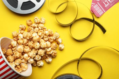 Sinema biletleri, patlamış mısır ve sarı arka planda film makaraları, düz konum