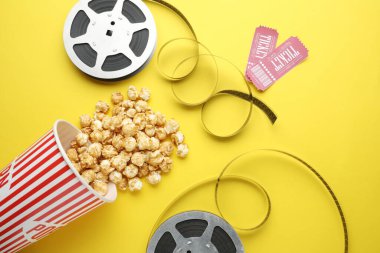 Sinema biletleri, patlamış mısır ve sarı arka planda film makaraları, düz konum