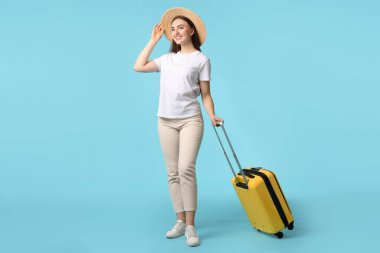 Açık mavi arka planda bavulu olan hasır şapkalı kadın.