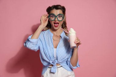 Pembe arka planda milkshake 'i olan heyecanlı kadın.