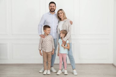Mutlu ebeveynler ve çocukları beyaz duvarın yanında.