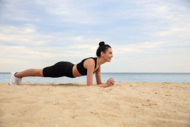 Sahilde tahta egzersizi yapan genç bir kadın. Vücut eğitimi