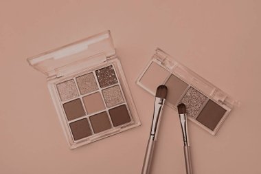 Göz farı paletleri koyu bej arka planda moka krem gözlüklü ve makyaj fırçaları düz yatıyordu. 2025 yılının moda rengi
