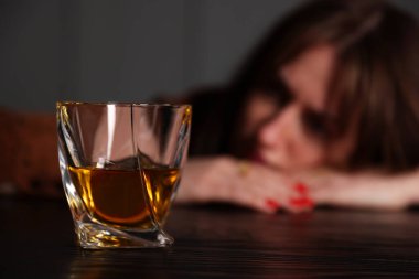 Alkol bağımlılığı. İçerideki ahşap masada oturan kadın, bir bardak viskiye odaklan.
