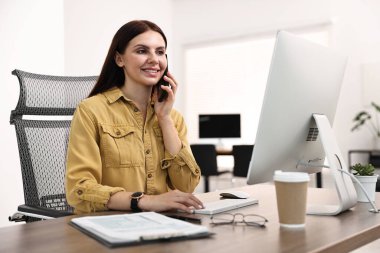 Ofiste çalışırken akıllı telefondan konuşan bir kadın.