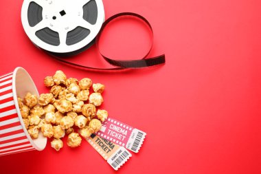 Tatlı patlamış mısır, sinema biletleri ve kırmızı arka planda film makarası.