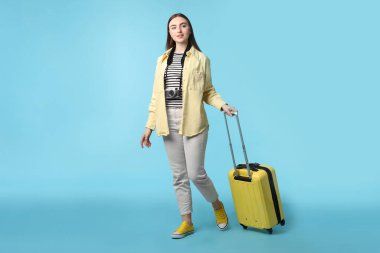 Klasik fotoğraf makinesi ve açık mavi arka planda bavulu olan kadın.