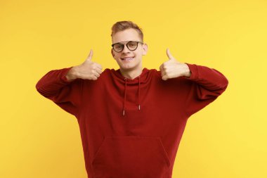 Sarı arka planda başparmak gösteren mutlu bir adam. Jest gibi