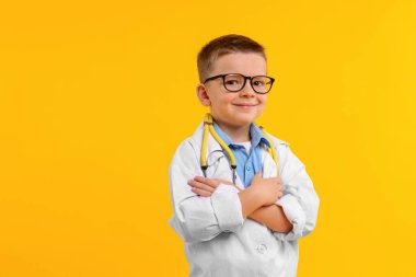 Steteskoplu küçük çocuk sarı arka planda doktor gibi davranıyor. Geleceğin mesleğini hayal etmek