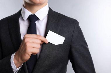 Gri arka planda ceketinin cebinden boş kartvizit alan adam, yakın plan. Tasarım için model