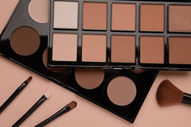 Kahverengi arka planda moka krem rengi paletler ve makyaj fırçaları, üst manzara. 2025 yılının moda rengi