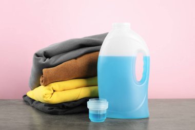 Çamaşır deterjanı şişede, kep ve giysiler gri masada.