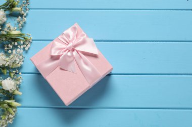 Güzel bir düğün hediyesi ve açık mavi ahşap masa üzerinde çiçekler, düz bir şekilde yatıyordu. Metin için boşluk