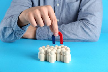 Man with magnet attracting wooden human figures on light blue background, closeup clipart