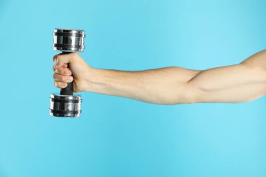 Açık mavi arka planda dambılla egzersiz yapan adam, yakın plan.