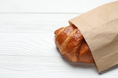Beyaz ahşap masanın üzerinde taze kruvasan olan kağıt torba, yakın plan. Metin için boşluk