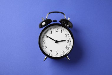 Mavi arkaplanda bir siyah alarm saati, üst görünümde.