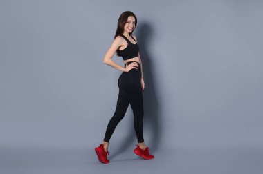 Gri arka planda şık spor kıyafetleri içinde güzel bir kadın.