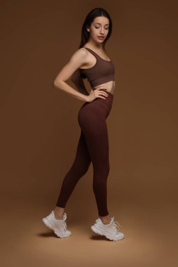 Kahverengi arka planda şık spor kıyafetleri içinde güzel bir kadın.
