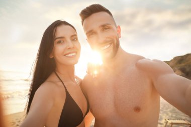 Mutlu genç çift gün batımında sahilde selfie çekiyor.