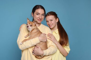 Genç kızı ve açık mavi arka planda şirin bir Chihuahua köpeği olan güzel bir annenin portresi.