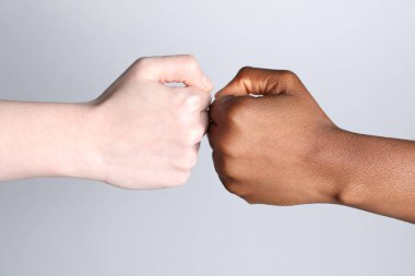 Stop racism. People of different skin colors bumping fists on light grey background, closeup clipart