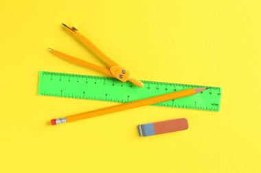 Sarı arka planda cetvel, kalem, pusula ve silgi düz.