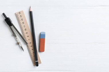 Cetvel, kalem, silgi ve pusula beyaz ahşap masada, düz yerde. Metin için boşluk