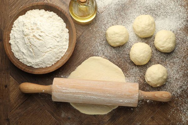 Fresh dough, rolling pin, flour and oil on wooden table, flat lay