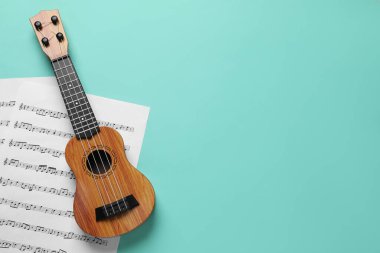Ukulele ve turkuaz arka planda müzik kağıtları, üst manzara. Metin için boşluk