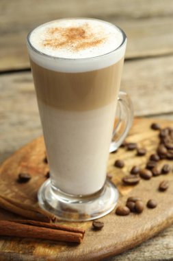 Cam bardakta latte macchiato, kahve çekirdekleri ve ahşap masada tarçın, yakın plan.