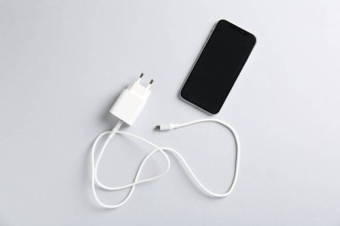 Beyaz arkaplanda şarj kablosu ve akıllı telefonu olan USB güç adaptörü, düz konum