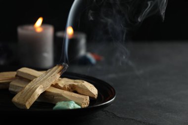 Yanan palo santo çubuğu, değerli taş ve siyah masada yanan mumlar, yakın plan. Metin için boşluk