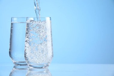 Açık mavi arkaplandaki bardaklara taze soda dökülüyor, yakın plan. Metin için boşluk